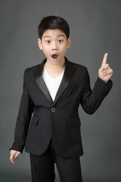 Liten asiatisk pojke i svart kostym pekar upp — Stockfoto