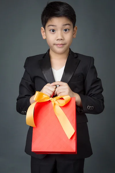 亚洲男孩穿黑色的西装，拿着礼品袋的肖像 — 图库照片