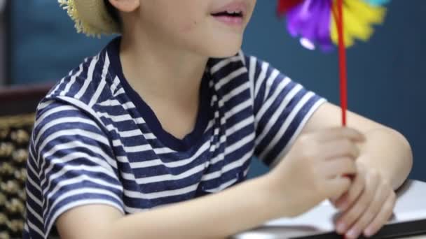 Little asian boy blows strongly on a plastic propeller, windmill and it turns quickly — Stock Video