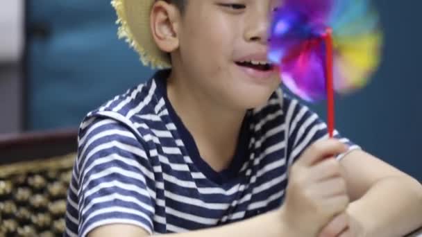 Little asian boy blows strongly on a plastic propeller, windmill and it turns quickly — Stock Video