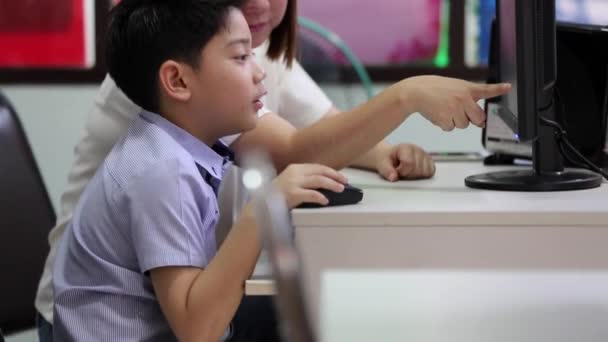 Asiático criança olhando para o computador na biblioteca com seu professor no ensino fundamental — Vídeo de Stock