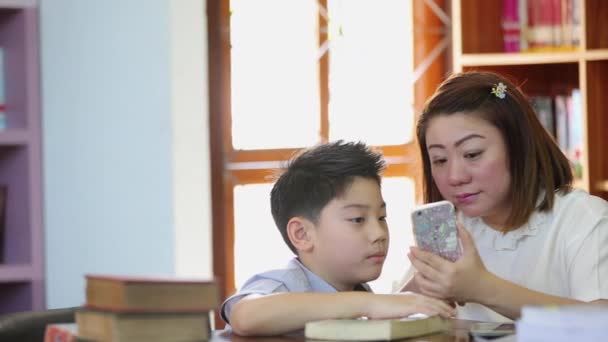 Happy asian boy and mother are take a photo by cell phone in library — Stock Video