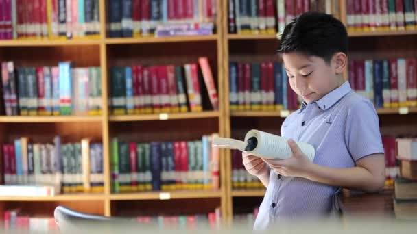 Pequeño asiático chico abeja aburrido con la lectura, biblioteca en tailandia — Vídeo de stock