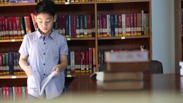 Pouco asiático menino abelha entediado com leitura, biblioteca em tailândia — Vídeo de Stock