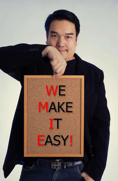 Asian man in black suit with WE MAKE IT EASY! message on wood board — Stock Photo, Image