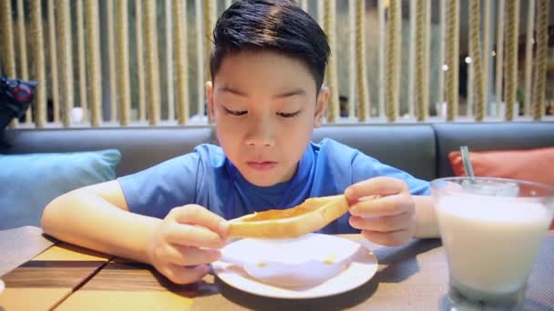 Щасливий азіатський хлопчик їсть шматочок хліба з посмішкою обличчя — стокове відео