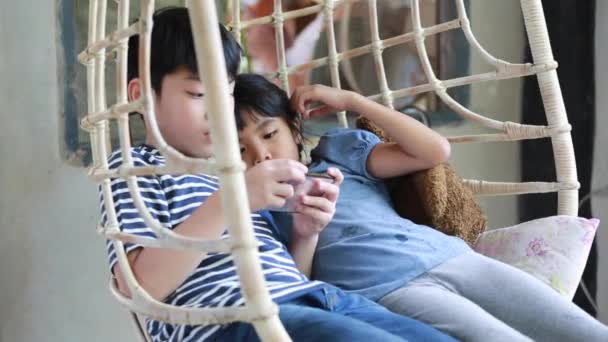 Little Asian boy and girl playing cell phone together in relax room — Stock Video