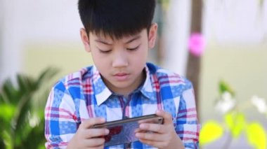 Oturma ve parkta akıllı cep telefonu kullanarak mutlu Asyalı çocuk