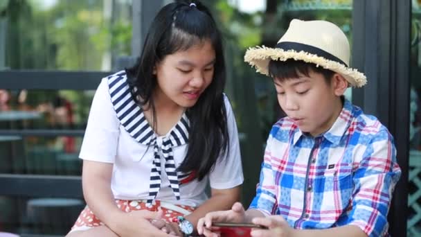 Aziatische jongetje met mobiele telefoon en tienermeisje praten samen — Stockvideo