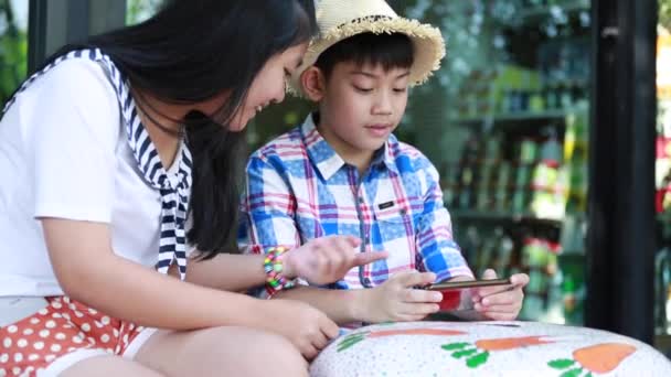 Little asian boy with mobile phone and teenage girl talk together — Stock Video