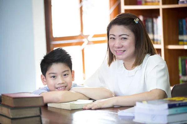Portrait of happy boy and teacher reading book by bookshelf in l — Stock Photo, Image