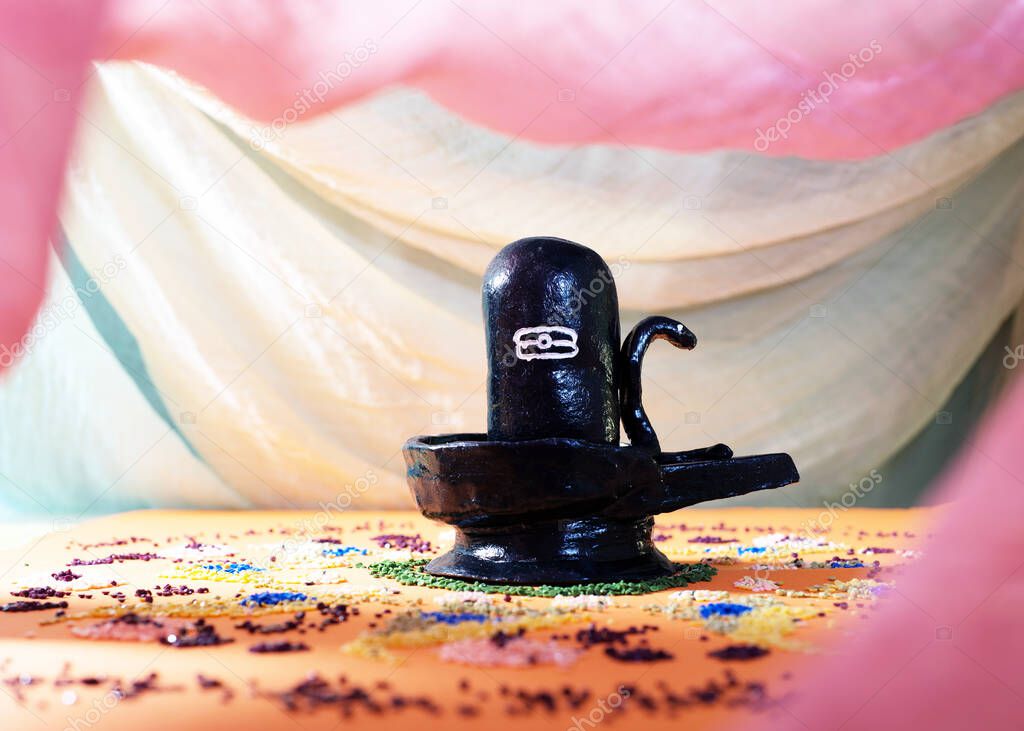 Black handmade Shiva Lingam figure with on an orange altar under curtains with roses