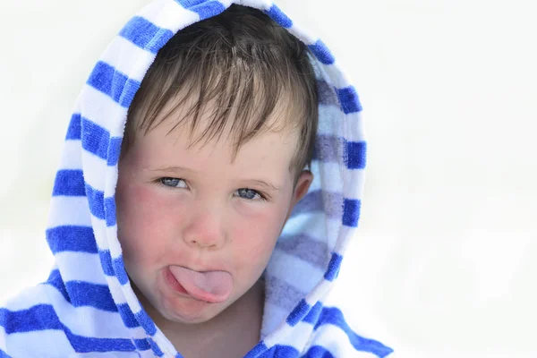 Hermoso bebé lindo con ojos azules en la túnica a rayas, burlas, mostrando la lengua, muecas, sobre un fondo blanco. Lindo niño con dermatitis atópica que muestra la lengua —  Fotos de Stock