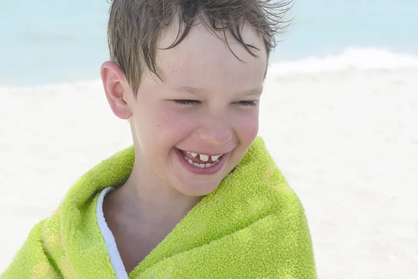 O menino na praia embrulhado em uma toalha, molhado depois de nadar — Fotografia de Stock