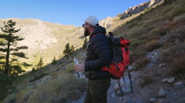 A man takes a refreshing break on a mountain trail, enjoying a cold drink while exploring the stunning beauty of the outdoors, perfect for adventure and travel