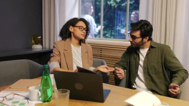 Modern bir ofiste, kendini işine adamış iki profesyonel, etkin çalışma uygulamaları ve başarılı proje sonuçları için takım çalışmasının hayati rolünü tartışıyor.