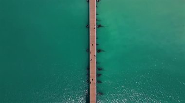 Şaşırtıcı hava görüntüleri güzel bir şekilde çeşitli seyahat ve manzara projeleri için mükemmel olan çarpıcı turkuaz sulara uzanan uzun ahşap bir iskeleyi sergiliyor.