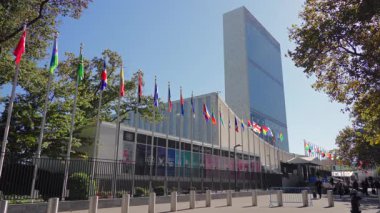 New York 10.28.2025. New York 'taki Birleşmiş Milletler Karargahı' nın manzarası. Parlak güneşli bir günde uluslararası bayraklar ve yeşil ağaçlarla çevrili..