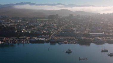 Morro Körfezi 'nin havadan görünüşü teknelerle sakin bir su, bir sahil kasabası ve yumuşak bir sabah ışığı uzak tepeler ve hafif sislerle çevrili huzurlu bir okyanus manzarası yaratıyor.