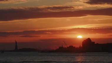 New York, New York 'ta gün batımında ufkun üzerinde parlayan ılık katmanlı bulutlar, suyun üzerinde yansıyan yumuşak ışık, sakin bir atmosferik kıyı anı yaratıyor.
