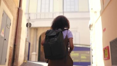 Sırt çantalı kadın turistin tarihi Avrupa caddesinde yürüyüşü, yumuşak gün ışığı ve eski mimari özgürlük, keşif ve huzur dolu tatil atmosferini ifade ediyor.