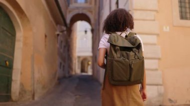 Sırt çantasıyla gezen genç bir bayan gezgin, tarihi binalarla dolu, parlak bir şehir caddesinde, bir kentsel seyahat merkezinin atmosferini yakalıyor..