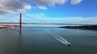 April Köprüsü 'nün havadan görüntüsü. Yüksek hız tekne oymacılığı kırmızı asma köprünün altında uyanır, beyaz sprey, dinamik su yolları, parlak gökyüzü ve enerjik deniz hareketleri spor için idealdir