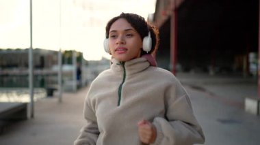 Sakin bir kadın kulaklıkla dışarıda koşuyor, müzik ve ritimle eğleniyor, kentsel alanda sürekli hareket ediyor, fitness yaşam tarzı, zihinsel berraklık, denge ve sağlıklı rutin