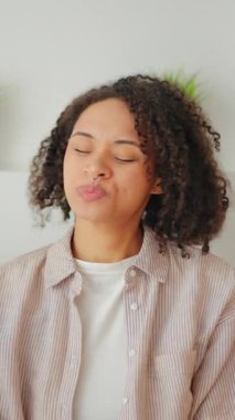 Evdeki kanepede oturan düşünceli bir kadın, gün ışığında sakin bir yaşam tarzı portresi, akıllı telefona, dekoratif yastıklara ve kapalı alanda huzurlu günlük atmosfere bakıyor..