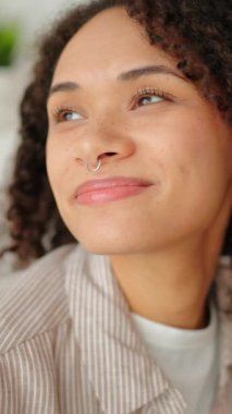 Gülümseyen kıvırcık kadın evinde dizüstü bilgisayarla koltukta oturuyor, rahat bir oturma odası iç mekanı, rahat yaşam tarzı, uzaktan çalışma konsepti, rahat, sakin, modern ev atmosferi.