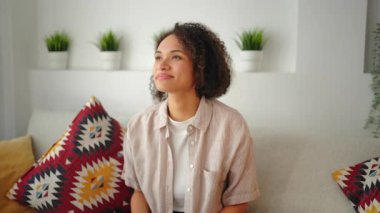 Evdeki bir kanepede otururken akıllı telefondan konuşan mutlu bir kadın. Doğal gün ışığı, rahat iç mekan ve neşeli günlük iletişim havası olan anlamlı bir yaşam tarzı..