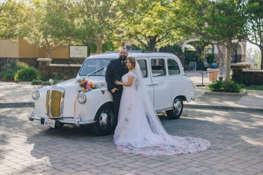 Sevinçli bir çift klasik bir düğün arabasının yanında gururla durur. Onları destekleyen aile ve arkadaşlarıyla çevrili unutulmaz özel günlerinde saf aşkı ve kutlamayı somutlaştırırlar.