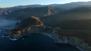Manzaralı Bixby Creek Köprüsü Big Sur California 'daki kanyon boyunca uzanır. Günbatımı ışığı, efsanevi 1. Otoyol boyunca engebeli uçurumları ve Pasifik kıyılarını vurguluyor..