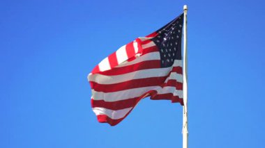 Birleşik Devletler bayrağının parlak gökyüzünün altında dalgalanması, vatanseverlik sembolü, özgürlük değerleri, ulusal gurur ve kültür mirası teması.