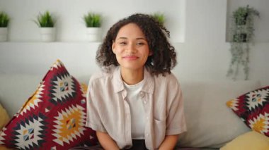 Evdeki bir koltukta otururken elinde uzaktan kumandayla gülümseyen kadın, rahat bir yaşam tarzı sahnesi doğal gün ışığı, rahat iç mekan, dekoratif yastıklar ve sakin bir ortam..