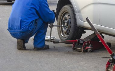 Tamirci vida değiştiriyor ya da söküyor. İngiliz anahtarı tamircisi iş yerinde bir arabanın tekerleğini değiştiriyor.