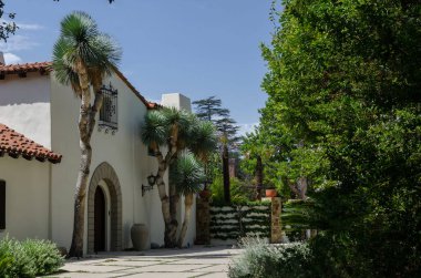 California Amerika Pasadena İspanyol tarzı bahçeli, ağaçlı, mavi gökyüzü, güneş ışığı ve sakin banliyö atmosferli beyaz villa.