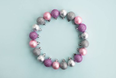 Noel partisi ve yeni yıl konsepti. Pastel açık mavi arka planda renkli Noel toplarından yapılmış bir çerçeve. Minimum bileşim. Üst görünüm, düz görünüm, kopyalama alanı