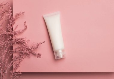 Cosmetic cream tube packaging on platform and flower branch on pastel pink background. Beauty and skincare concept, mockup for design. Minimal trendy composition. Top view, flat lay, copy space
