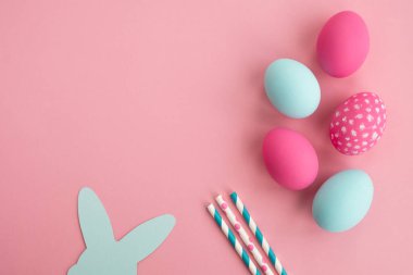 Colorful easter eggs and bunny rabbit ears made of paper on light pink background. Minimal composition in pastel colors. Top view, flat lay, copy space