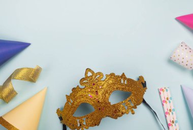 Karnaval maskesi ve açık mavi arka planda şenlik süslemeleri. Parti, Mardi Gras veya Purim bayramı. Üst görünüm, düz görünüm, kopyalama alanı