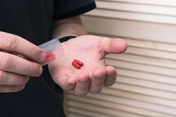 Evde elinde plastik şişeyle kırmızı haplar tutan bir adam. Sağlık, tıp konsepti. Kapat.
