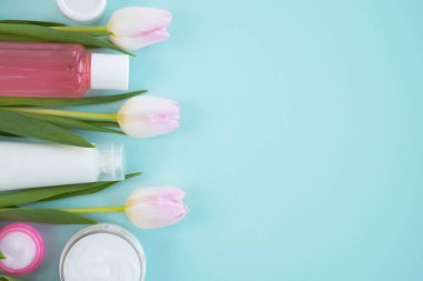 Açık mavi arka planda kozmetik ürünleri ve çiçek laleleri. Güzellik kavramı, cilt bakımı. Üst görünüm, düz görünüm, kopyalama alanı