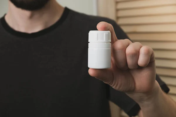 Man holding in hand plastic bottle with pills. Health, pharmaceuticals and medicine concept. Close up