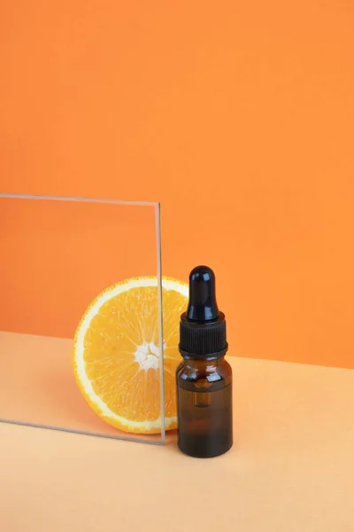 Vitamin C serum glass bottle or citrus essential aroma oil on orange background. Contemporary still life, minimal composition. Natural organic cosmetics concept. Vertical