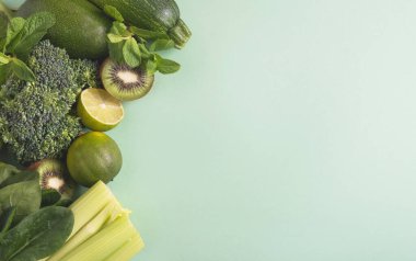 Yeşil sebzeler ve hafif arka planda meyveler. Brokoli, ıspanak yaprağı, avokado, kabak, kereviz, limon, kivi çeşitleri. Temiz yemek konsepti, sağlıklı beslenme. Üst görünüm, düz görünüm, kopyalama alanı