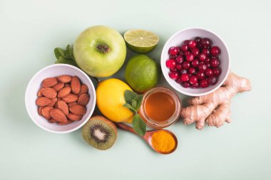 Yeşil arka planda bağışıklık geliştirmek için sağlıklı yiyecekler. Limon, bal, kızılcık, zencefil kökü, kivi, elma, nane, fındık ve zerdeçal. Sağlık, vitaminli ürünler, virüs önleme. Üst manzara, düz uzanma