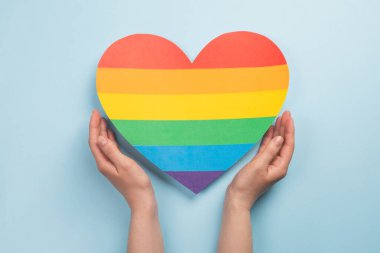 Kadınların elleri açık mavi arka planda gökkuşağının renginde kalbi tutar. LGBT konsepti, Gurur ayı. Üst görünüm