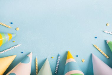 Doğum günü partisi geçmişi. Pastel mavi yüzeyde karnaval şapkaları, konfetiler ve mumlar. Üst görünüm, düz görünüm, kopyalama alanı