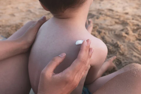 Anne, küçük çocuğa güneş kremi sürüyor. Plajda SPF güneş kremi, cilt konsepti. Kapat.